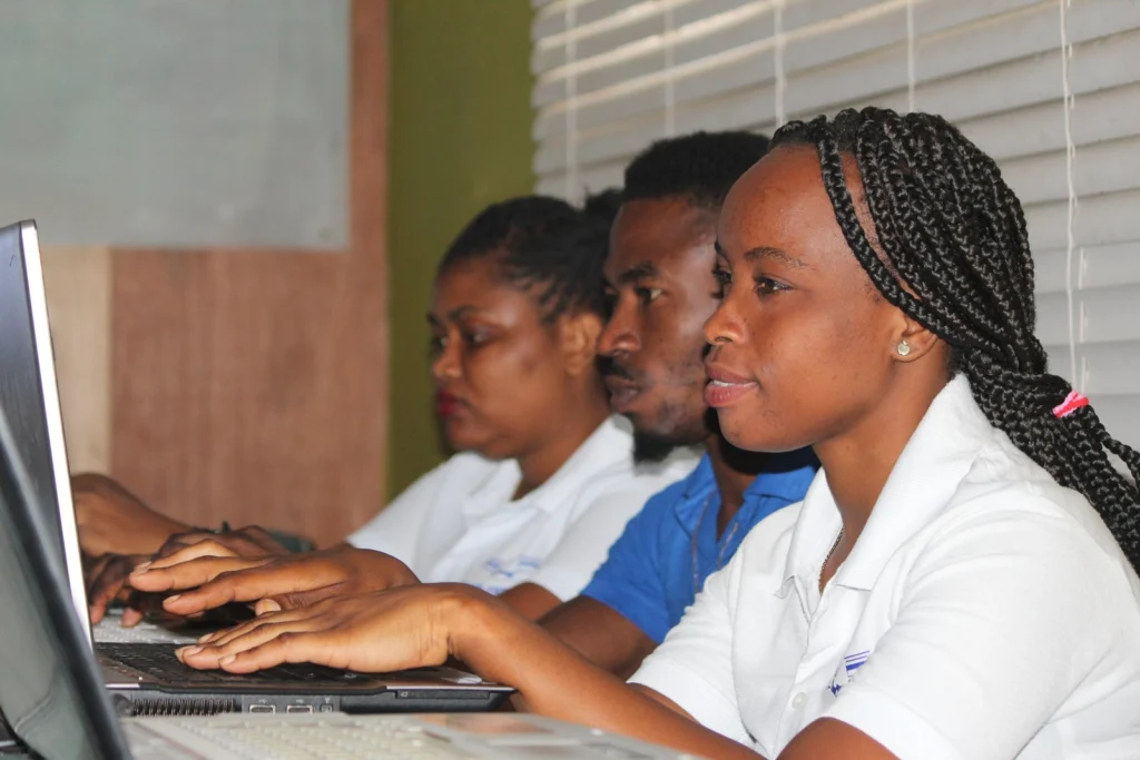 Étudiante tapant sur le clavier de son ordinateur portable, entourée d’autres étudiants